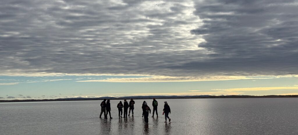 A group walking across a shining salt lake under a cloudy sky